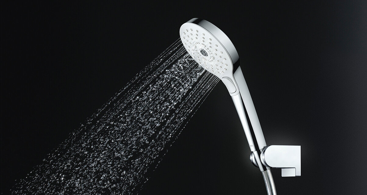 Vor einem schwarzen Hintergrund ist ein Duschkopf abgebildet. Aus diesem kommen Wasserstrahlen heraus. Die Wasserstrahlen der äußeren Öffnungen sind dünn und gerade. Die inneren der Wasserstrahlen sind spiralförmig. 