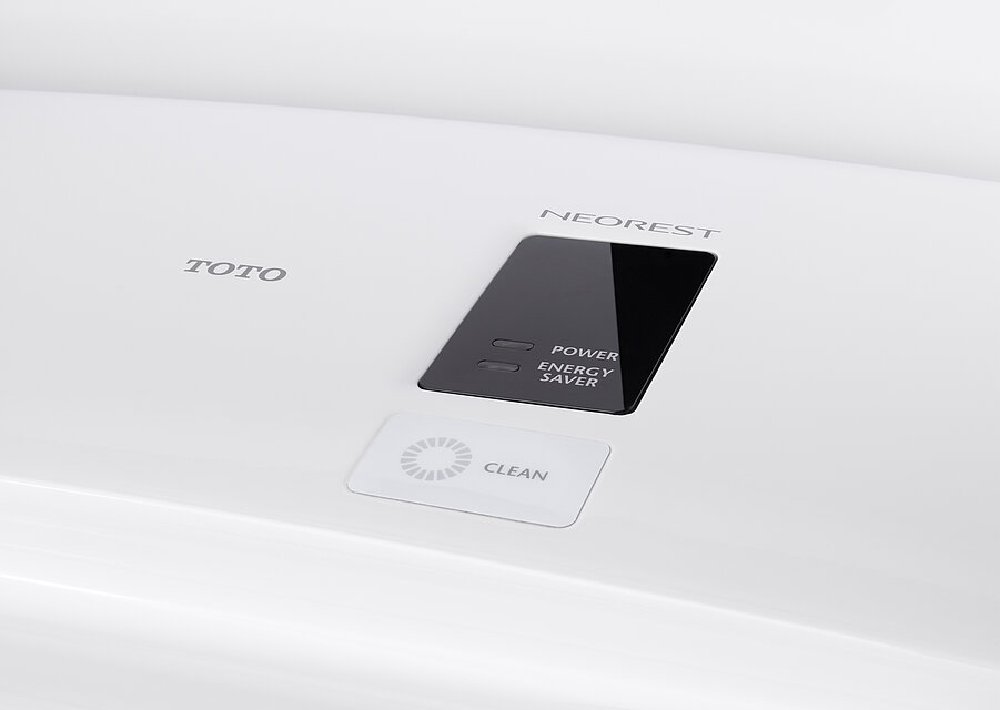 Man sieht eine Detailaufnahme der Anzeige auf der Oberseite des Washlet. In einem schwarzen Kasten stehen die Worte „Power“ und „Energy Saver“ neben zwei ausgeschalteten Lampen. Darüber befindet sich der Schriftzug „Neorest“, links daneben der Schriftzug TOTO und darunter in einem weißen Kasten der Schriftzug „Clean“ neben einem grauen Kreis.